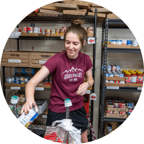 Volunteer sorting food items in a pantry, wearing an NMSU shirt.